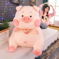 Large cute pig plush toy with a heart pendant, displayed on a sofa next to a smiling woman in a cozy room setting.