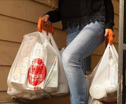 Woman using MAMMOTH GRIP Heavy Duty Carrier to carry multiple grocery bags up stairs, showcasing its strength and ergonomic design.