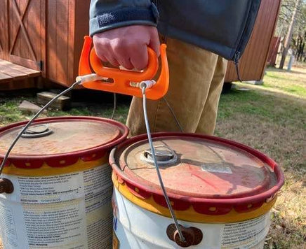 Person carrying two large buckets with MAMMOTH GRIP Heavy Duty Carrier, perfect for industrial and home improvement use.