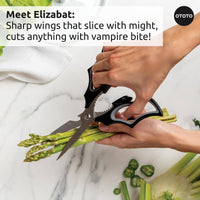 Halloween Bat Kitchen Scissors - OTOTO Elizabat Shears cutting asparagus on marble counter. Bat-wing shaped handles add spooky charm to kitchen tasks.
