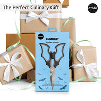 OTOTO Elizabat Halloween Bat Kitchen Scissors in gift packaging, surrounded by wrapped presents. Ideal spooky-themed culinary gift.