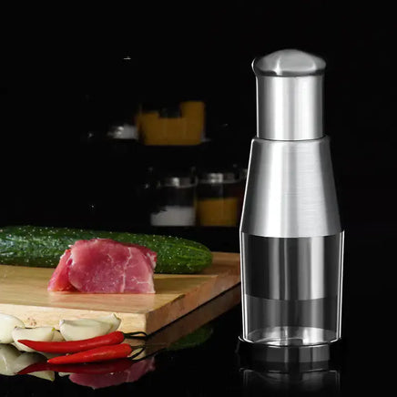 Stainless steel garlic crusher and onion chopper placed on a kitchen counter beside fresh ingredients, highlighting its sleek design.