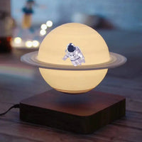 Levitating Saturn lamp with an astronaut figure on its surface, glowing warmly on a wooden base.