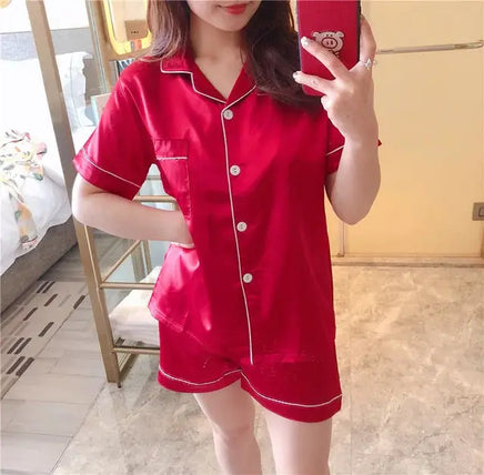 Women's silk satin pajamas in vibrant red with white piping, featuring a short-sleeve button-up top and matching shorts for luxurious comfort.