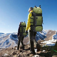 Two hikers wearing green 90L outdoor travel backpacks, trekking through a snowy mountain landscape, showcasing its outdoor utility.