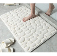 White super absorbent shower room floor mat with a pebble-like texture, placed near a shower area with slippers nearby.