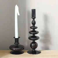 Two black Rue glass candlesticks, one with a white taper candle, displayed on a wooden surface with a neutral gray background.