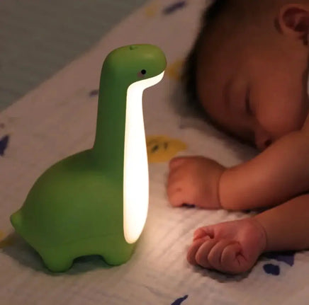 Green dinosaur night light illuminating softly beside a sleeping baby, ideal for creating a cozy and comforting atmosphere in a child's room.