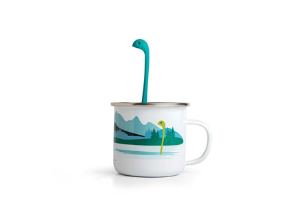 Cute Tea Infuser by OTOTO shaped like a sea monster, placed in a white enamel mug with a lake and forest design. Fun tea accessory for loose leaf tea.