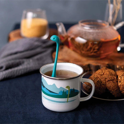 Cute Tea Infuser by OTOTO shaped like a blue sea monster in a white enamel mug with mountain design, perfect for loose leaf tea lovers.