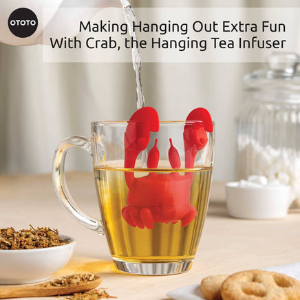 Cute Tea Infuser by OTOTO shaped like a red crab hanging on a glass mug, steeping loose leaf tea. A fun tea accessory for kitchen or gift use.