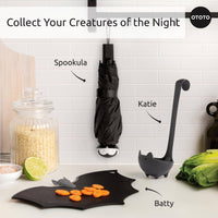 OTOTO Halloween kitchen gadgets including Spookula bat umbrella, Katie black cat ladle, and Batty bat-shaped cutting board on white counter.
