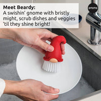 Beardy Gnome Dish Brush by Ototo scrubbing a plate with strong bristles, ideal for cleaning dishes and vegetables with ease.