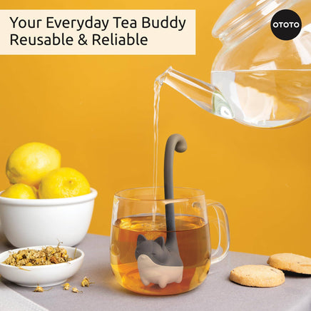 Cute Tea Infuser by OTOTO shaped like a cat soaking in a glass mug of tea, ideal for loose leaf brewing. Fun tea accessory with a long handle design.