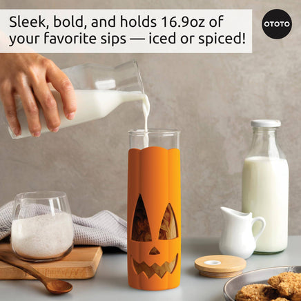 Pumpkin-themed Halloween glass tumbler being filled with milk, showcasing its 16.9oz capacity for iced or spiced drinks.
