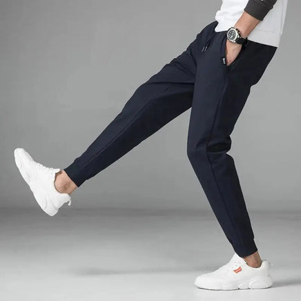 Crossfit Track Sweatpants showcasing a sleek black design with tapered fit, ideal for gym and casual wear. Styled with white sneakers for a sporty look.