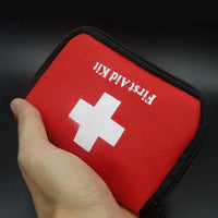 Hand gripping a red first aid kit bag with a white cross, emphasizing its portability and convenience for emergencies.