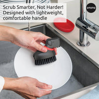 Oscar Dog Dish Brush by Ototo shown wet after use, resting in its red tray, perfect for scrubbing dishes and vegetables.