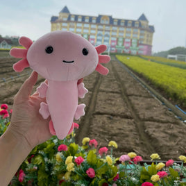 Pink anime axolotl plush toy held in front of a scenic garden and large building, perfect for gifting or collecting.