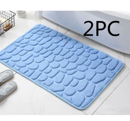 Blue super absorbent shower room floor mat with a pebble-like texture, sold as a 2-piece set, placed near a bed and slippers.