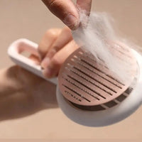 Hand peeling off collected pet hair from the pink Automatic Hair Remover & Massage Comb, highlighting its easy cleaning feature.