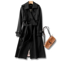 Elegant black trench coat featuring a double-breasted style, adjustable belt, and plaid lining, styled with a tan handbag.