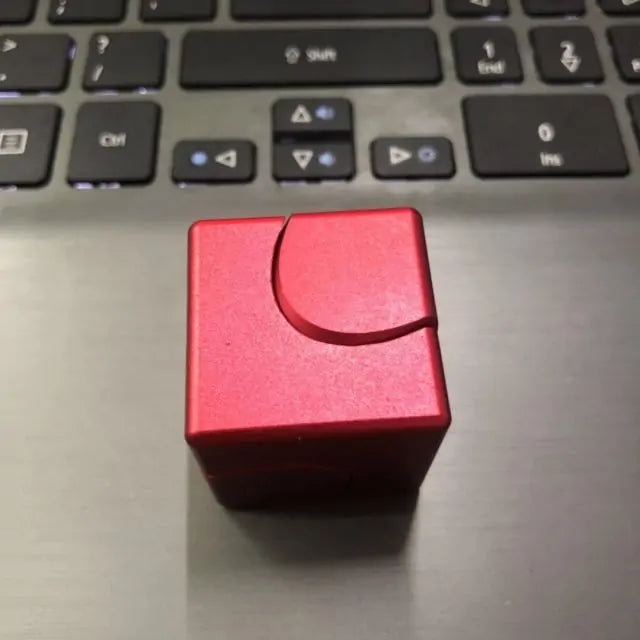 Red metallic fidget spinner cube placed on a laptop, featuring a smooth finish and ergonomic design for stress relief.