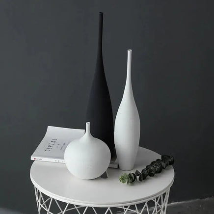 Three Jingdezhen modern minimalist handmade vases in black and white on a round white table, styled with books and greenery.