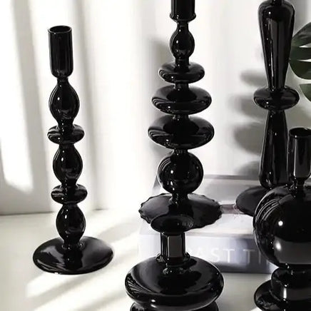 Assorted black Rue glass candlesticks with unique designs, arranged on a white surface with natural light and a decorative book.