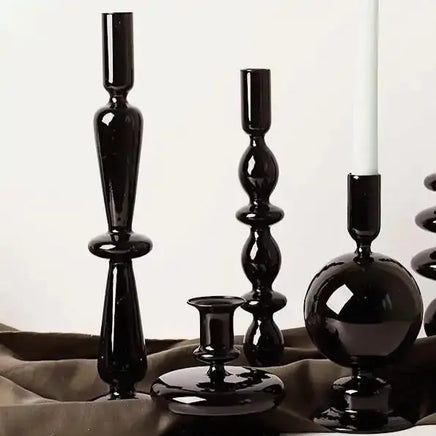 Elegant black Rue glass candlesticks in varying shapes, styled on a brown fabric for a sophisticated home decor look.