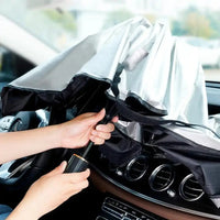 Foldable car sunshade being collapsed by a user, showcasing its reflective silver and black heat-resistant material.