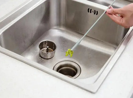 Sewer dredger tool removing debris from a kitchen sink drain, showcasing its claw mechanism for efficient clog removal.