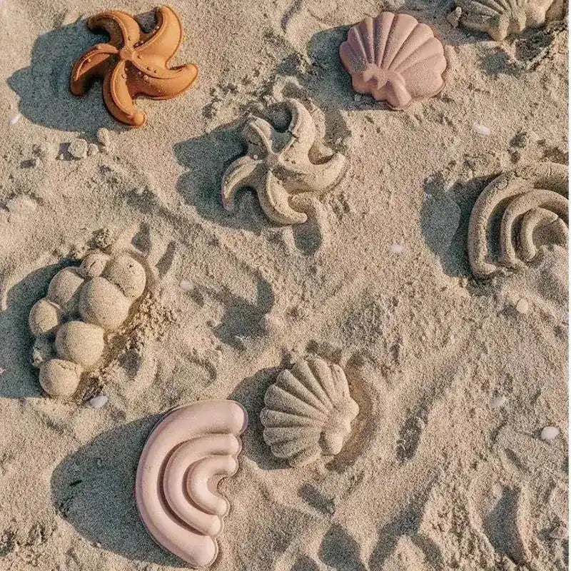 Various sand molds in starfish, shell, and rainbow shapes imprinted on the beach, perfect for creative seaside playtime.