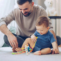 Father and toddler enjoying playtime with a sensory toy featuring colorful pull strings, promoting bonding and developmental skills.