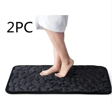 Black super absorbent shower room floor mat with a pebble-like texture, sold as a 2-piece set, featuring a person stepping on it.