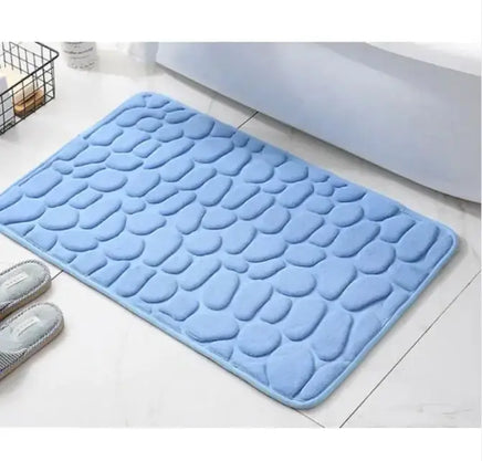 Blue super absorbent shower room floor mat with a pebble-like texture, placed near a bed and slippers.