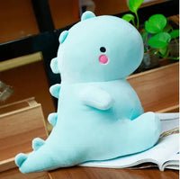 Light blue dinosaur plush toy with soft fabric and adorable design, displayed on a wooden desk with plants in the background.