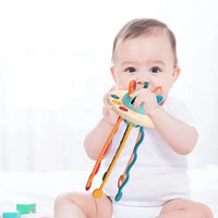 Baby holding a sensory toy with colorful pull strings, engaging in tactile exploration and motor skill development.