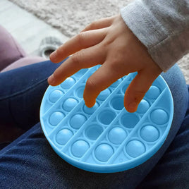 Child pressing a blue round silicone push bubble fidget toy on their lap, ideal for stress relief and sensory play.