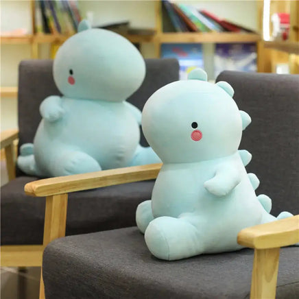 Two light blue dinosaur plush toys sitting on gray chairs in a cozy room with bookshelves in the background.