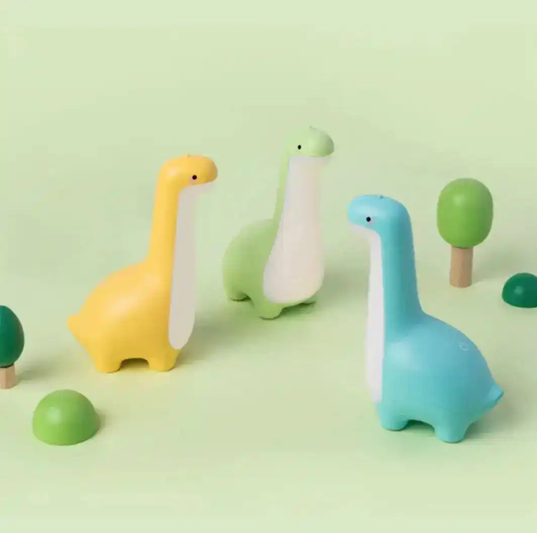 Set of three dinosaur night lights in yellow, green, and blue, surrounded by toy trees, perfect for playful and ambient light