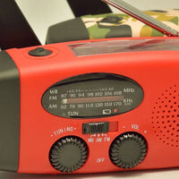 Close-up of the red emergency radio's AM/FM/WB tuning dials, frequency display, and solar panel.