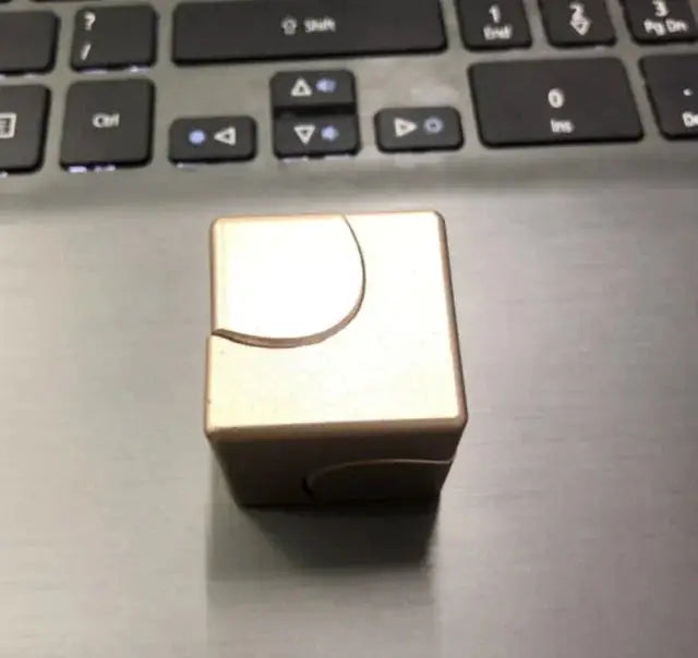 Gold metallic fidget spinner cube on a laptop, highlighting its smooth finish and stress-relief capabilities.