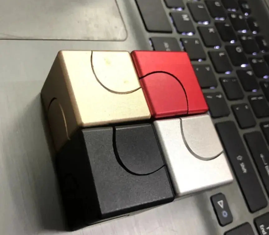 Set of four metallic fidget spinner cubes in gold, red, black, and silver, arranged on a laptop for stress relief and focus enhancement.