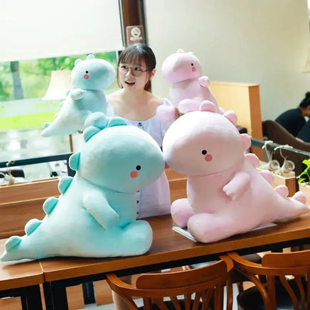 Collection of pink and blue dinosaur plush toys in various sizes, displayed on a table with a woman admiring them.