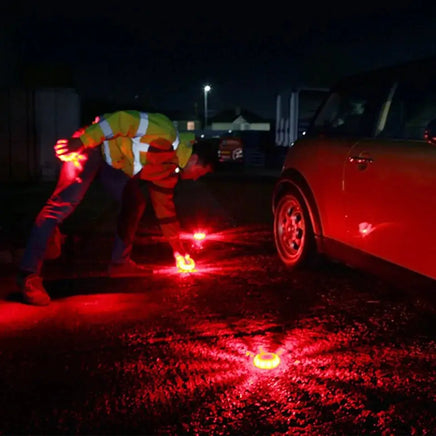 Person placing red LED emergency car lights on the road at night to enhance visibility and ensure roadside safety.