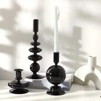 Black Rue glass candlesticks in modern shapes, styled on a white surface with a book and minimalist decor accents.