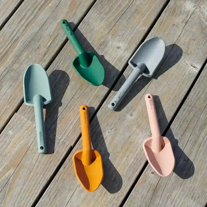 Colorful plastic beach shovels in green, grey, yellow, and pink, perfect for digging and building sandcastles at the seaside.