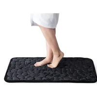 Black super absorbent shower room floor mat with a pebble-like texture, featuring a person stepping on it.