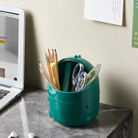 Green dinosaur desktop trash can repurposed as a pen holder on a marble desk, showcasing multifunctional home office use.